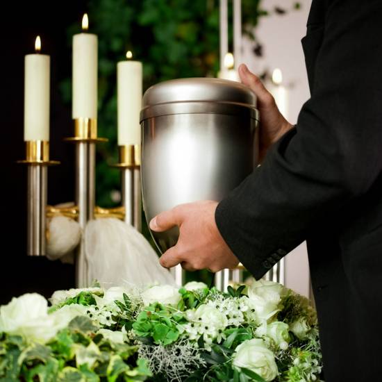 Grief – urn Funeral and cemetery death and dolor - funeral and cemetery, mortician carrying the urn to a bed of white roses